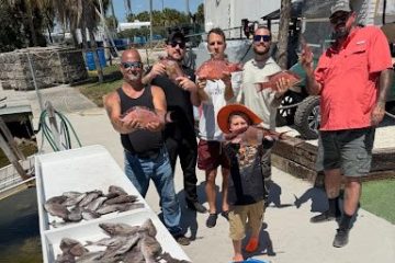 Group of people posing with a table full of freshly caught fish outdoors.