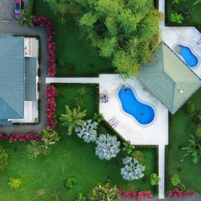 Aerial view of two houses and two pools surrounded by green lawns and trees.
