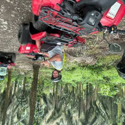 Group of people riding red ATVs on a forest path, one person smiling at the camera.